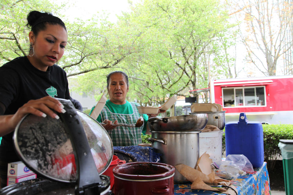 In this Tuesday, April 15, 2014 photo, worker Julliana Rojas, left, helps Mixteca Catering owner Paula Asuncion to serve tamales with traditional Oaxacan mole sauce at the Lloyd Farmers Market in Portland, Oregon. Asuncion once worked in the fields, but after participating in a micro-business development program she now sells tamales throughout Portland and has even hired others to help in the business. (AP Photo/Gosia Wozniacka)