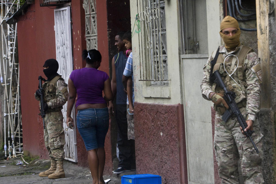 Masked police officers stand guard as residents stand in the doorway of their home in downtown Colon, Panama, Saturday, Oct. 20, 2012. Police began patrolling Colon after violent protests Friday over a new law allowing the sale of state-owned land to private companies already leasing land there to handle the import and export of goods in the duty-free zone next to the Panama Canal. Protesters want the government to instead raise the rent and invest the money in Colon, a poor and violent city. (AP Photo/Arnulfo Franco)