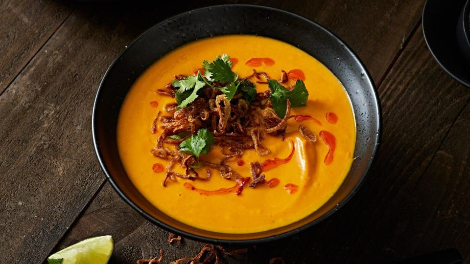 bowl of carrot ginger soup topped with crispy shallots, chili oil, and cilantro