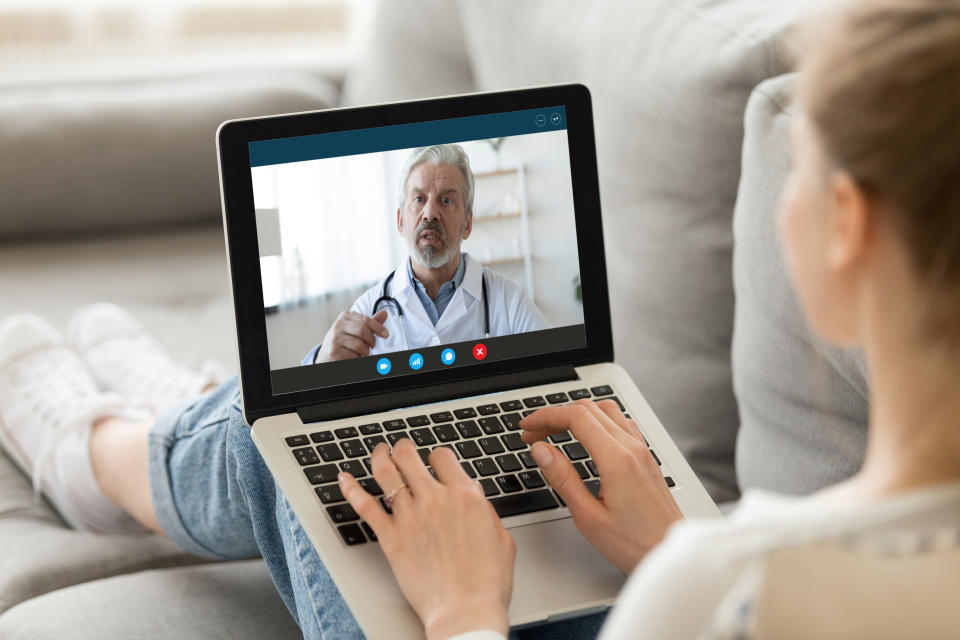 Young woman sit on couch at home have video call with doctor use wireless internet connection on laptop, female patient talk consult with physician online on webcam conference on computer