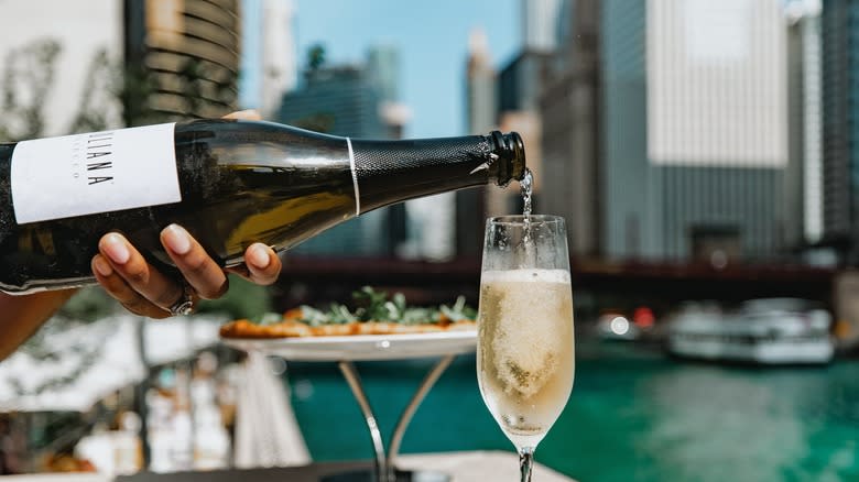 champagne poured in glass with pizza and city in background