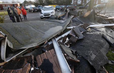 Residents watch a car damaged by a blown away rooftop of a building in the coastal town of Cuxhaven at the North Sea, December 6, 2013. REUTERS/Fabrizio Bensch