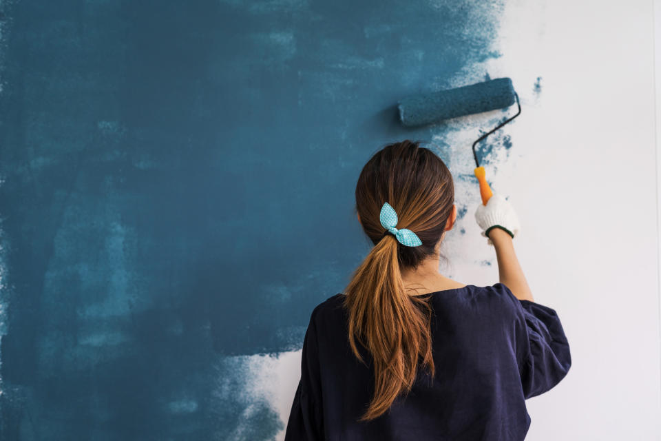 A woman painting a wall with blue paint.