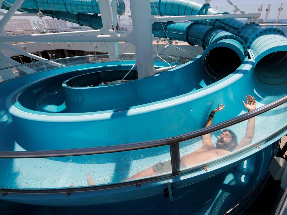 This image shows a blue waterslide with a man sliding down it with his hands in the air.