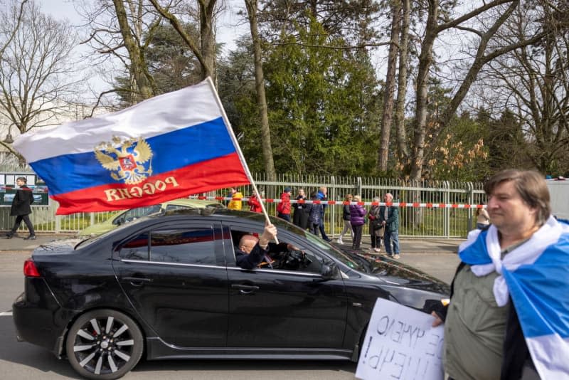 A man holds a Russian flag out of the window of a car drives past the Russian Consulate General during the 2024 Russian presidential elections. Thomas Banneyer/dpa
