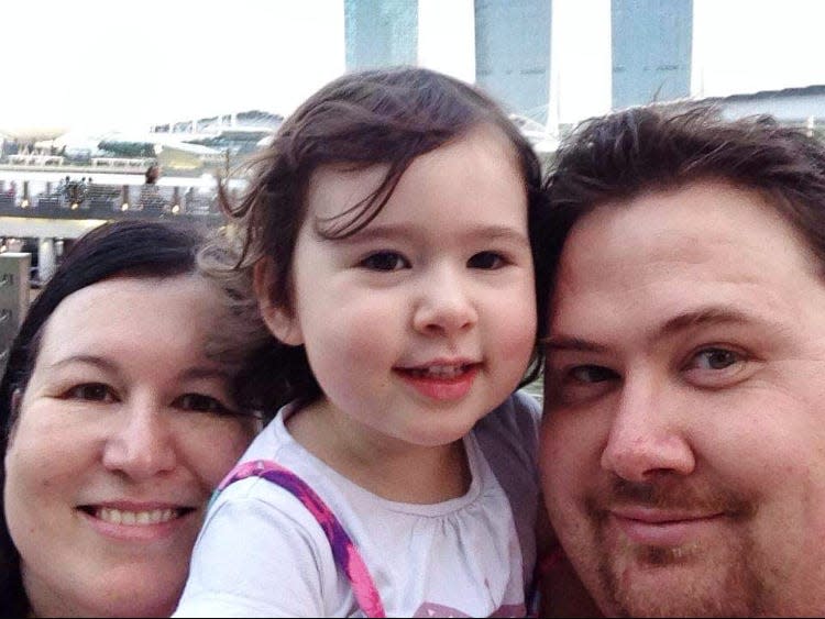 A family of three — a mom, dad and little girl — posing for a selfie.
