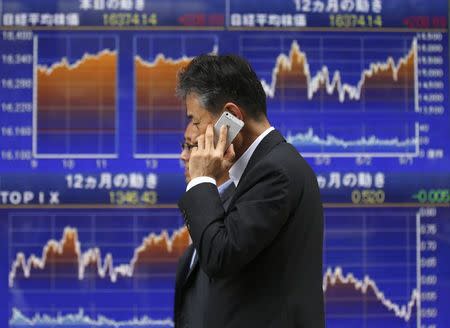 Men walk past an electronic board showing Japan's Nikkei average (above), outside a brokerage in Tokyo September 25, 2014. REUTERS/Toru Hanai