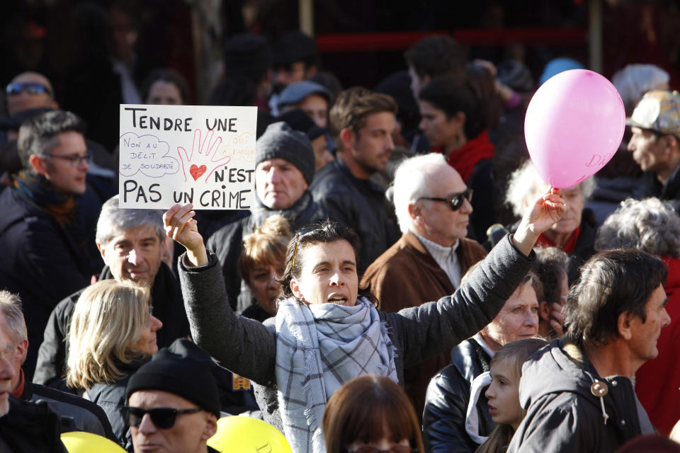 This Jan. 4, 2017 photo shows a woman holding a placard reading "Holding one's hand out is not a crime", as she supports Cedric Herrou, a French activist farmer who faces up to five years in prison as he goes on trial accused of helping African migrants cross the border from Italy, in Nice, southern France. A French appeals court is expected to hand down a verdict Thursday afternoon in the case of a mountain guide who was convicted for helping migrants enter the country illegally. (AP Photo/Claude Paris, File)