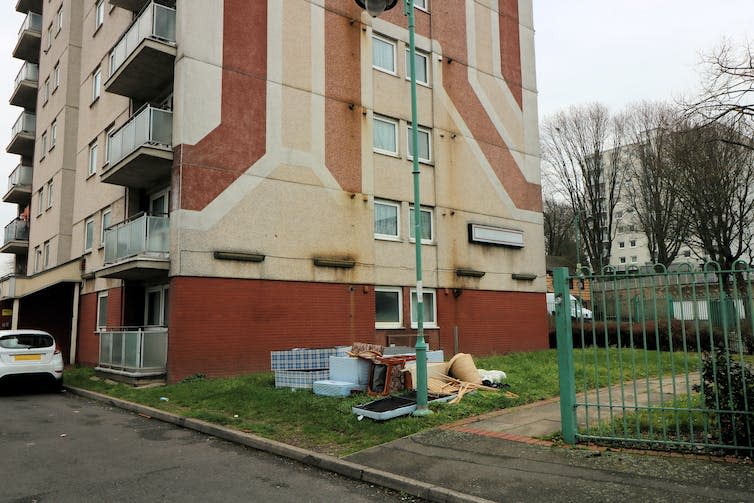 A high-rise building with ochre coloured murals and a patch of grass with a green railing.