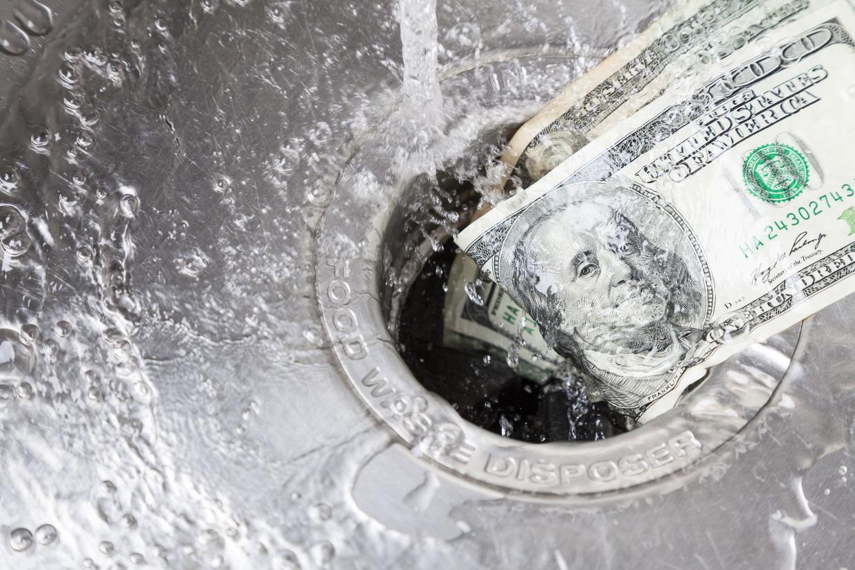 A one hundred dollar bill and a twenty dollar bill being washed by water down the drain, with water droplets everywhere