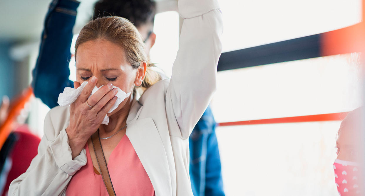 Woman sneezing with cold on train. (Getty Images)