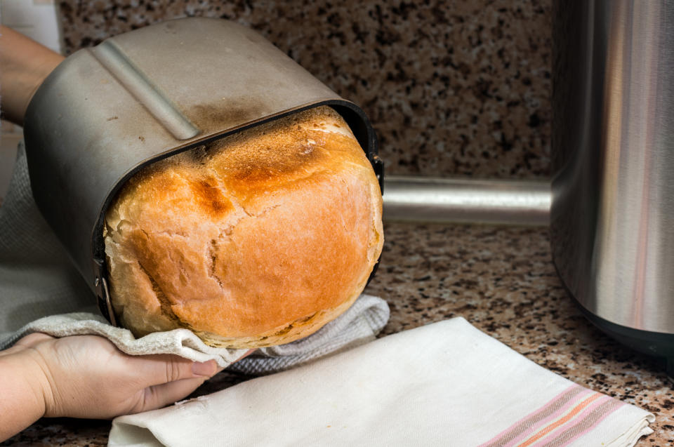Person removing freshly baked loaf of bread from a metal bread maker