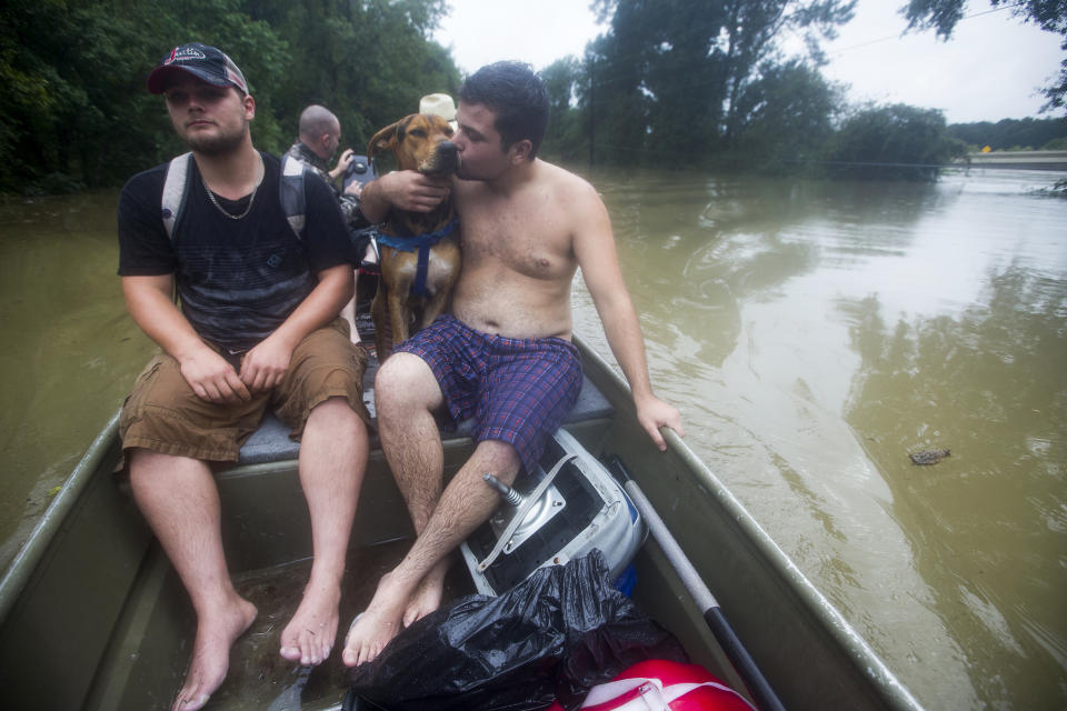 Jerran Pearson, left, and Ryan Bettencourt and his dog, Chief, are rescued by boat from their neighborhood flooded due to heavy rain spawned by Tropical Depression Imelda on Thursday, Sept. 19, 2019, in Patton Village, Texas. (Brett Coomer/Houston Chronicle via AP)