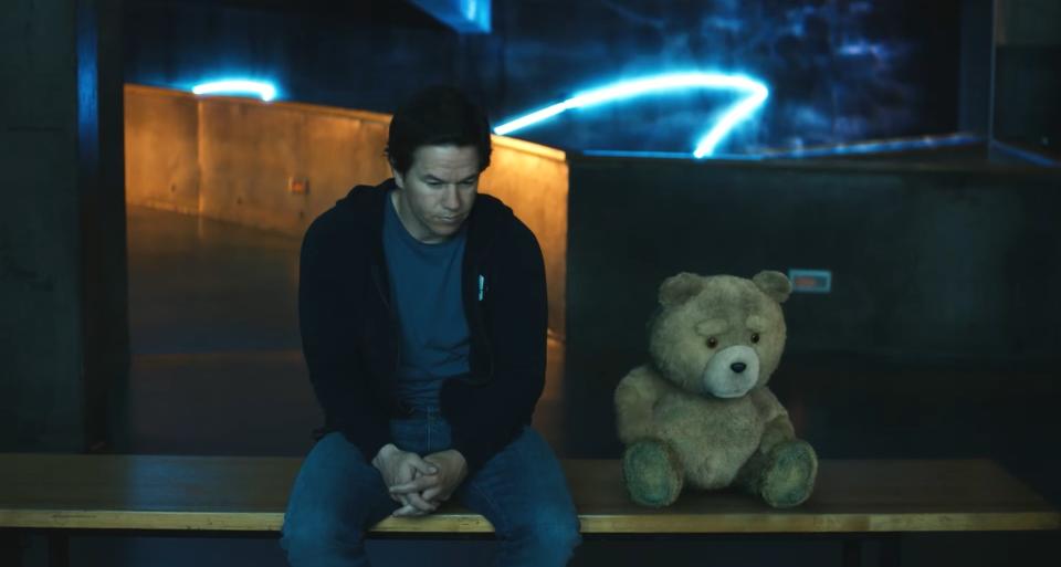 A man and his friend, who is a talking teddy bear, sit outside