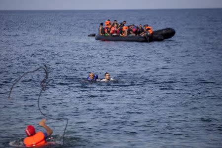 A man throws a rope to Syrian refugees swimming towards a beach after abandoning a dinghy with a broken engine on the Greek island of Lesbos, September 9, 2015. REUTERS/Dimitris Michalakis