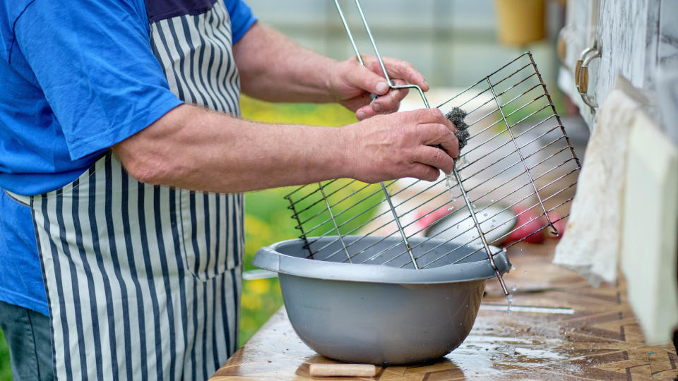 Someone cleaning a grill grate in a bowl of water