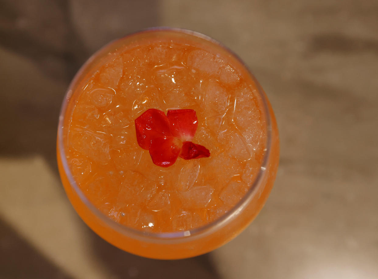 An orange cocktail seen from above, decorated with some red flower petals. 