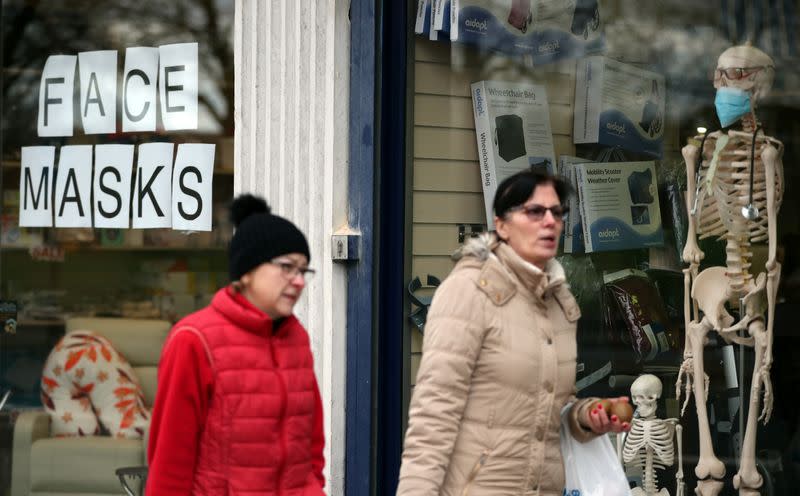 People walk past the window of a medical equipment supply store advertising the sale of protective masks in south London