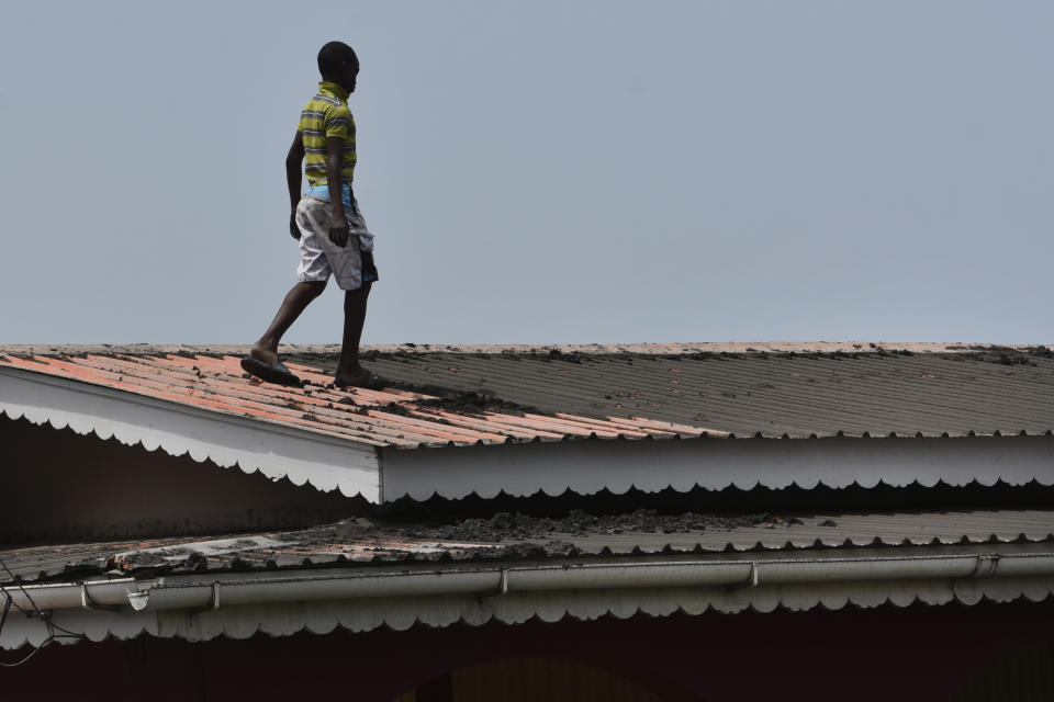 A youth walks on the roof of a home covered in volcanic ash after La Soufriere volcano erupted, in Wallilabou on the western side of the Caribbean island of St. Vincent, Monday, April 12, 2021. (AP Photo/Orvil Samuel)
