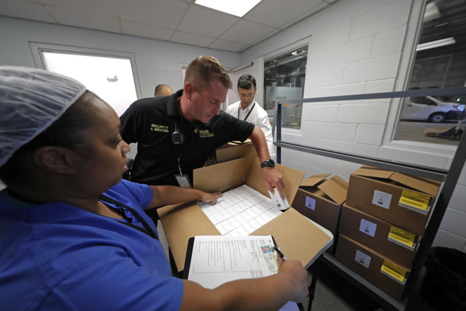 Shira Betts, an employee of GB Sciences Louisiana, readies the first ever boxes of legal medical marijuana in the state, as a private security guard inspects the contents, as it is readied for transport, in Baton Rouge, La., Tuesday, Aug. 6, 2019. (AP Photo/Gerald Herbert)