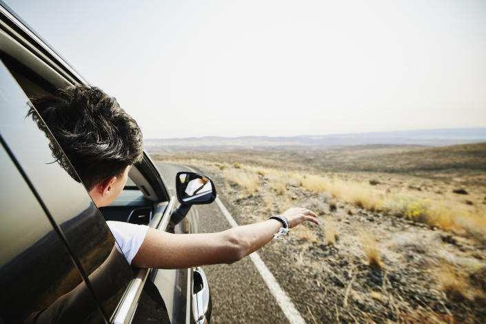 Person leaning out of passenger seat window while driving. Weekend travel, road trip concept