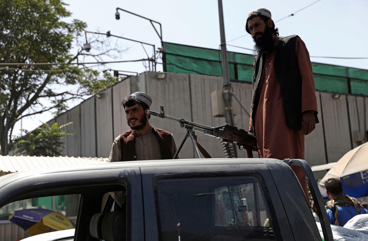 Taliban fighters stand guard on the back of a vehicle with a machine gun in front of the main gate leading to the Afghan presidential palace, in Kabul, Afghanistan, Monday, Aug. 16, 2021.