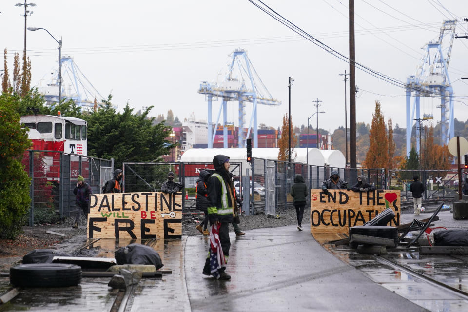 Protesters hold signs up in front of train tracks leading into the Port of Tacoma as activists delay the loading of the Cape Orlando vessel, Monday, Nov. 6, 2023, in Tacoma, Wash. (AP Photo/Lindsey Wasson)