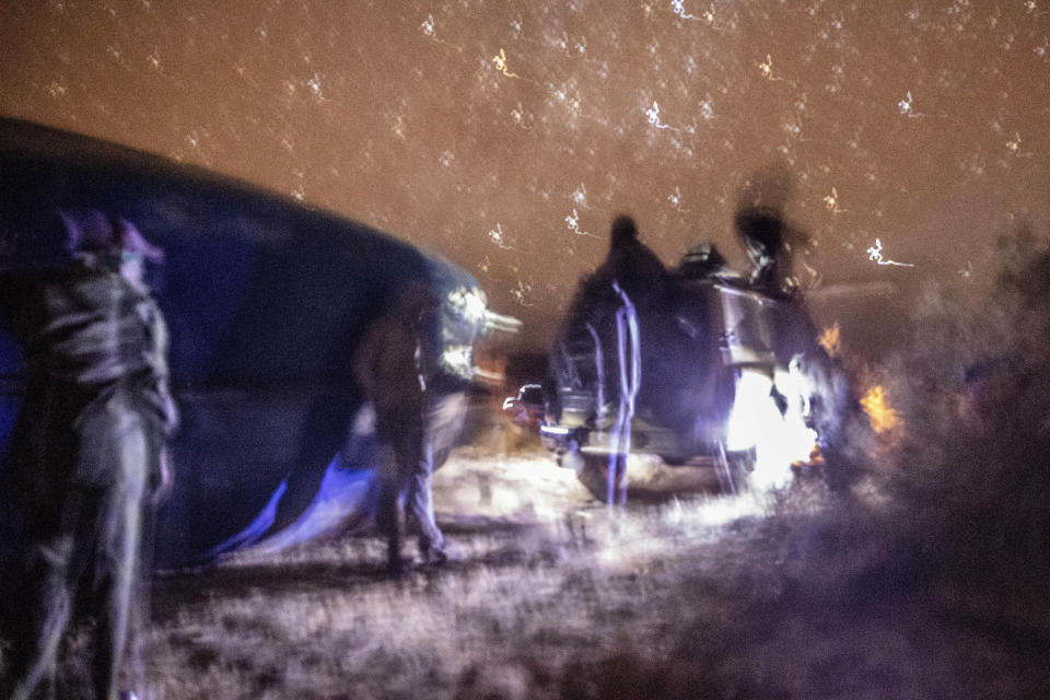 Smugglers gather near and pause atop a vehicle as they attempt to lift a fishing boat in a remote desert out of the town of Dakhla in Morocco-administered Western Sahara, Tuesday, Dec. 22, 2020. (AP Photo/Mosa'ab Elshamy)