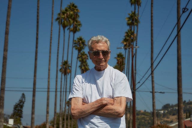 Derek Boshier stands with his arms folded and wearing a white T-shirt