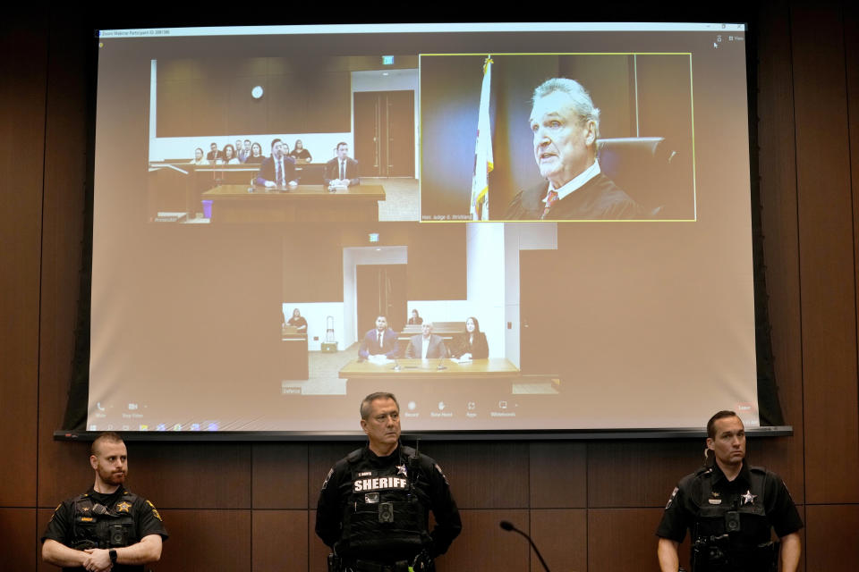 Lake County Ill., law enforcement officers stand under a projection of Judge George D. Strickland as Strickland address the court during the appearance of Robert E. Crimo Jr., father of Robert Crimo III, at the Lake County, Ill., Courthouse Thursday, Jan. 26, 2023, in Waukegan, Ill. Crimo Jr., faces seven counts of felony reckless conduct for signing the application for his son's firearm owners ID card in December of 2019. (AP Photo/Nam Y. Huh, Pool)