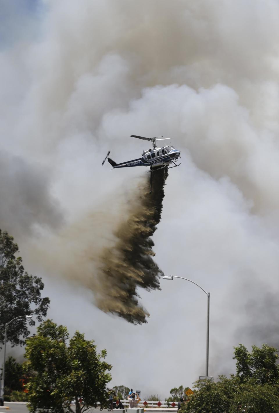 Un helicóptero arroja un líquido retardante sobre un incendio forestal el miércoles 14 de mayo de 2014 en Carlsbad, California. Las llamas impulsadas por el viento amenazan las casas en la ciudad costera de Carlsbad, donde las autoridades enviaron avisos para evacuar más de 11.000 casas y establecimientos. (Foto AP Photo)