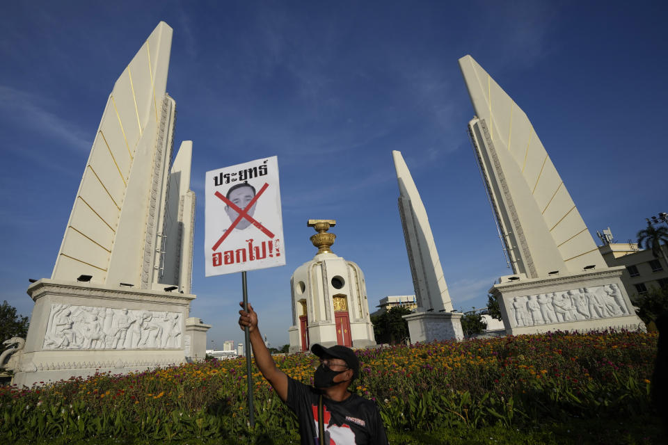 An anti-government protester holds poster which reads "Prayuth get out" in front of Democracy Monument in Bangkok, Thailand Tuesday, Aug. 23, 2022. Thailand Constitutional Court on Monday received a petition from opposition lawmakers seeking a ruling on whether Prayuth has reached the legal limit on how long he can remain in office. (AP Photo/Sakchai Lalit)