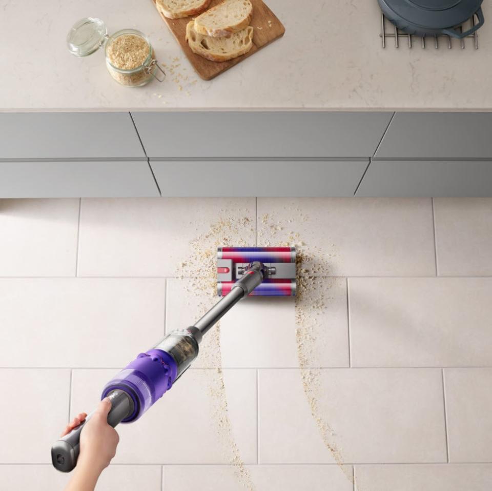 Person using a cordless vacuum cleaner to pick up crumbs on a kitchen floor