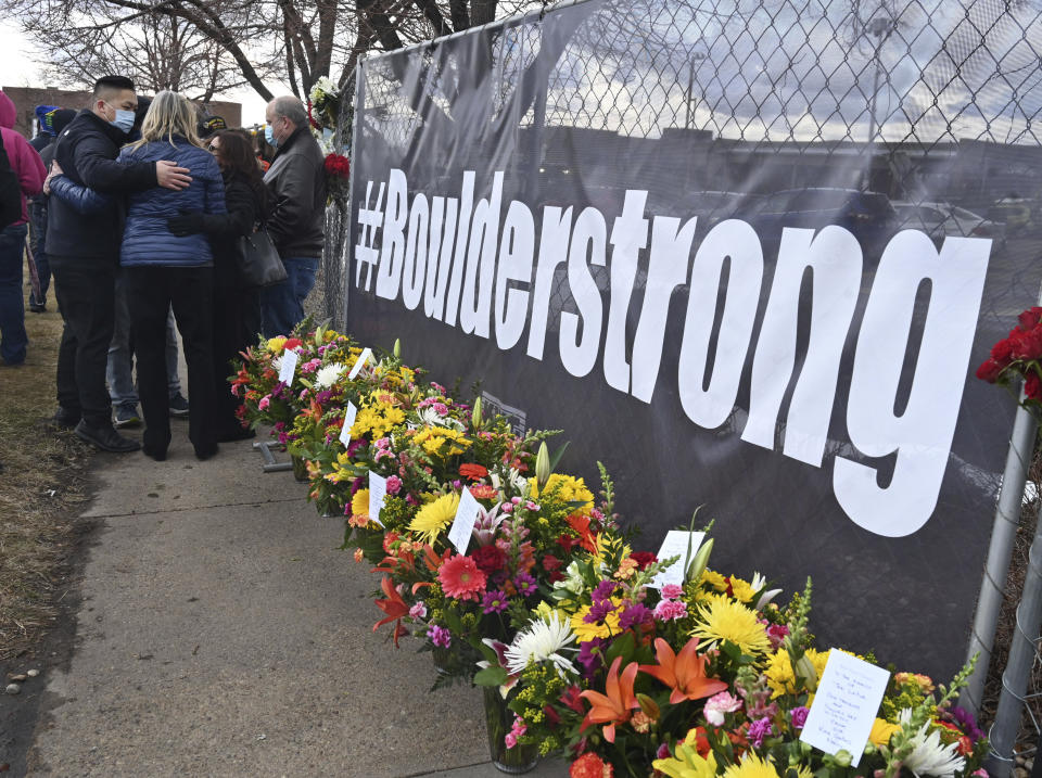 A solemn group of King Soopers employees, left, some from the Boulder store and some from the same district brought large sprays of flowers for each of the victims of a mass shooting at a Boulder Kings Soopers store on Monday. Each spray had a card with condolences for the victims' families and signed by their King Sooper family. The group brought their flowers to a fence around the King Soopers where a makeshift memorial has been made for the ten victims of a mass shooting. Tuesday, March 23, 2021. (Jerilee Bennett/The Gazette via AP)