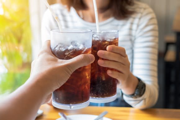 A woman clinking a glass of soda with another person