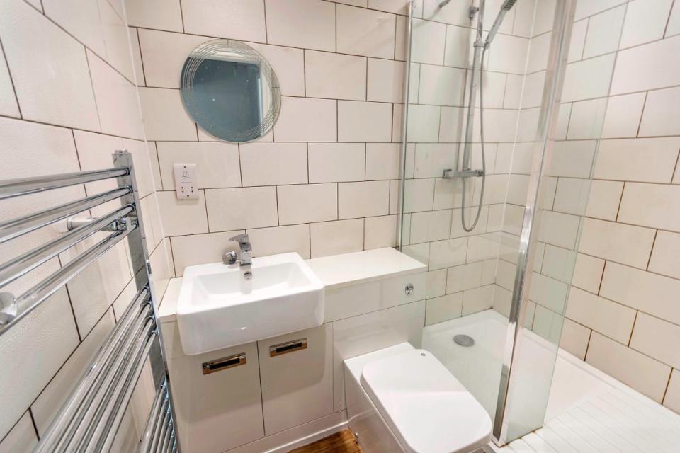 The three-piece bathroom suite if modern and fully-tiled in white, comprising of shower cubicle, vanity unit handwash basin with storage cupboards beneath. It also has a ladder towel radiator, wood-effect flooring and spotlights.