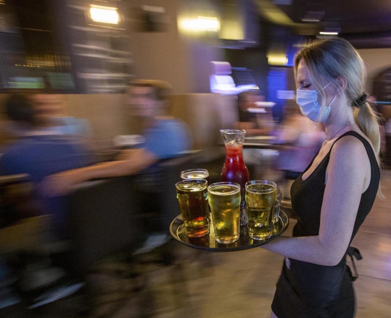 <span class="caption">A waitress wears a mask while carrying drinks for guests inside the Blu Martini restaurant in Kingston, Ont., in July 2021. </span> <span class="attribution"><span class="source">THE CANADIAN PRESS/Lars Hagberg </span></span>