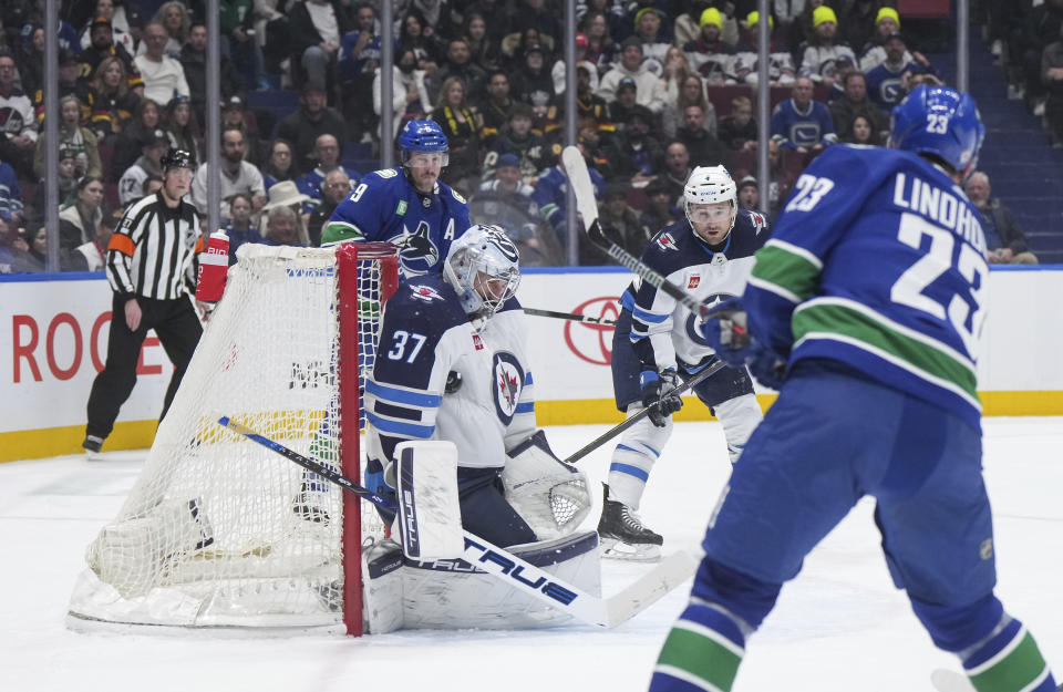 Winnipeg Jets goalie Connor Hellebuyck (37) stops Vancouver Canucks' Elias Lindholm (23) during the first period of an NHL hockey game in Vancouver, British Columbia, Saturday, Feb. 17, 2024. (Darryl Dyck/The Canadian Press via AP)