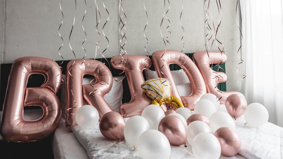 Beautiful balloons on a bed in a hotel room spelling the word bride.