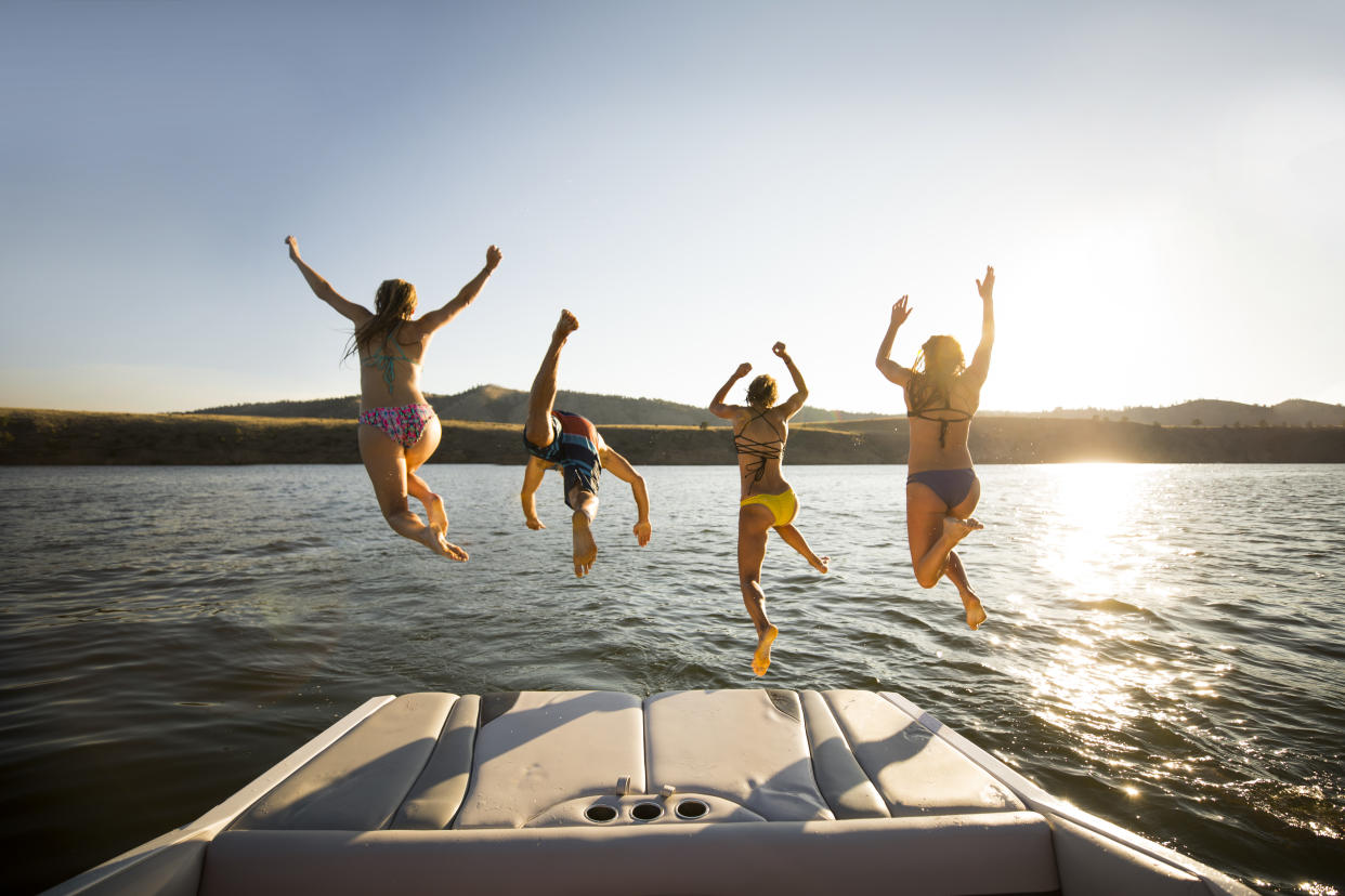 Four friends jumping into a lake off the back of their boat.