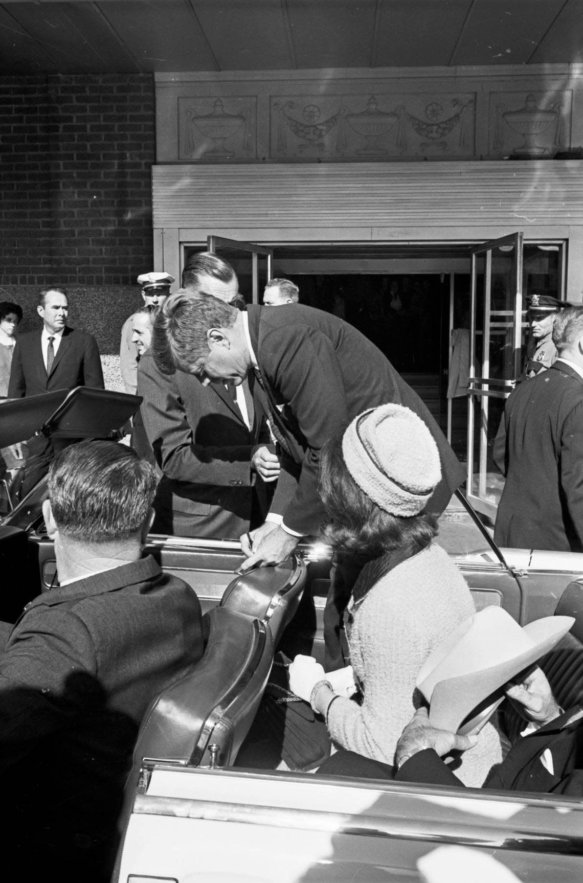 President John F. Kennedy signing an autograph with Jackie Kennedy at his left and Gov. John Connally in the motorcade limousine outside of Hotel Texas. The motorcade drove down Main Street on the way to Carswell Air Force Base. Nov. 22, 1963