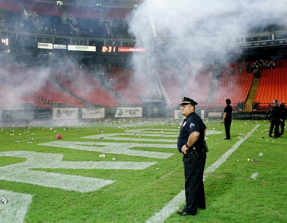 Denver Police Department officers stand in the north end zone of Denver's Mile High Stadium as a cloud of tear gas envelopes the stadium late Saturday, Sept. 4, 1999, after police used the gas to disperse fans who wanted to storm the field to celebrate Colorado State's 41-14 victory over Colorado. Fans pelted police and then Colorado players as they left the field for the locker room beneath the stands.
