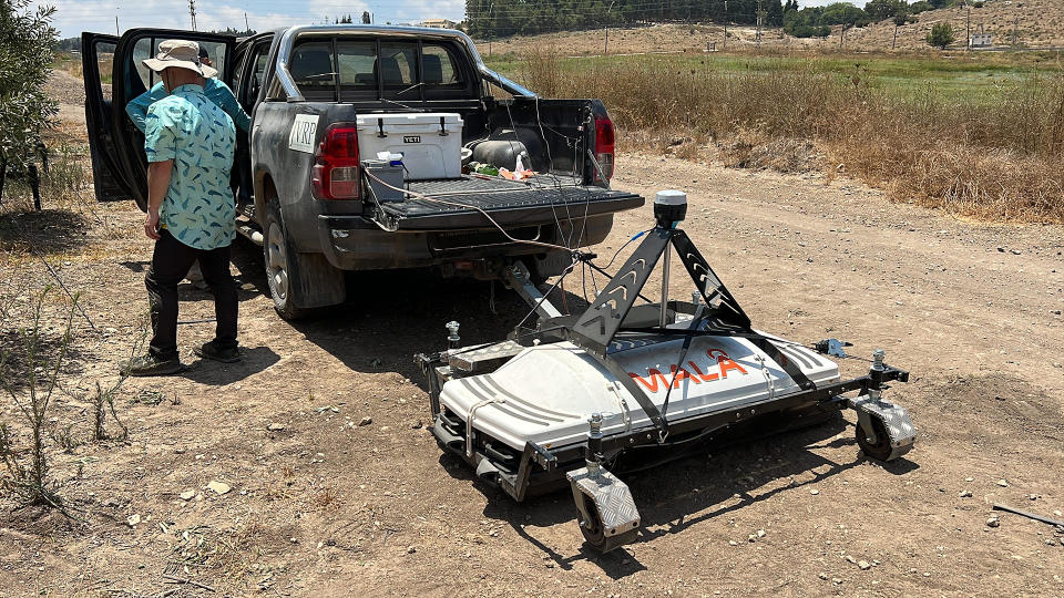 We see a pickup truck parked on the dirt. It is pulling a rectangular ground-penetrating radar system.