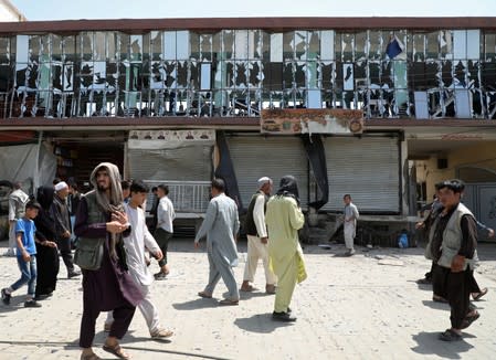 People walk in front of a building with broken windows at the site of a car bomb blast in Kabul