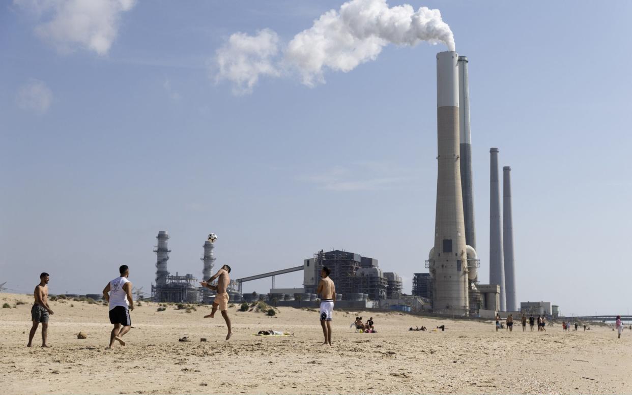 Young Israelis play football on the beach near the Orot Rabin power station