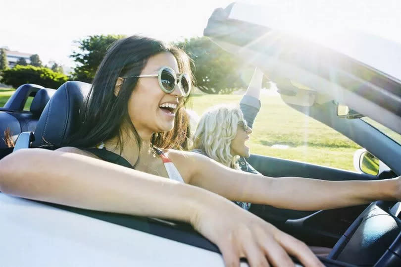 Excited women driving convertible on road trip