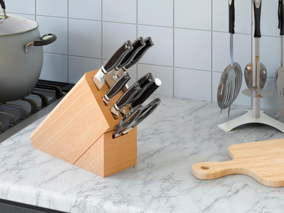 A collection of many kitchen knives in wooden block on granite countertop