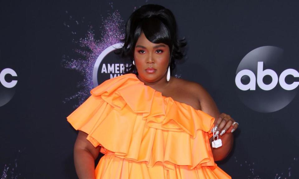 Lizzo at the American Music Awards, in an orange off-the shoulder ruffle, layered dress and holding a tiny Valentino bag between her fingers.