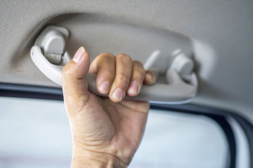 Cropped human hand holding handle in the car.