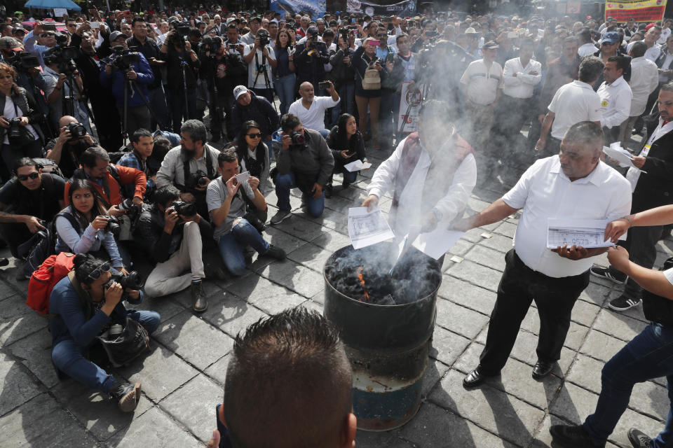 Taxi drivers symbolically burn photo copies of their license plates to protest ride apps, in Mexico City, Monday, Oct. 7, 2019. The protesters want the apps banned, arguing that the apps are unfair competition because those drivers are more loosely regulated and don't have to pay licensing fees. (AP Photo/Marco Ugarte)